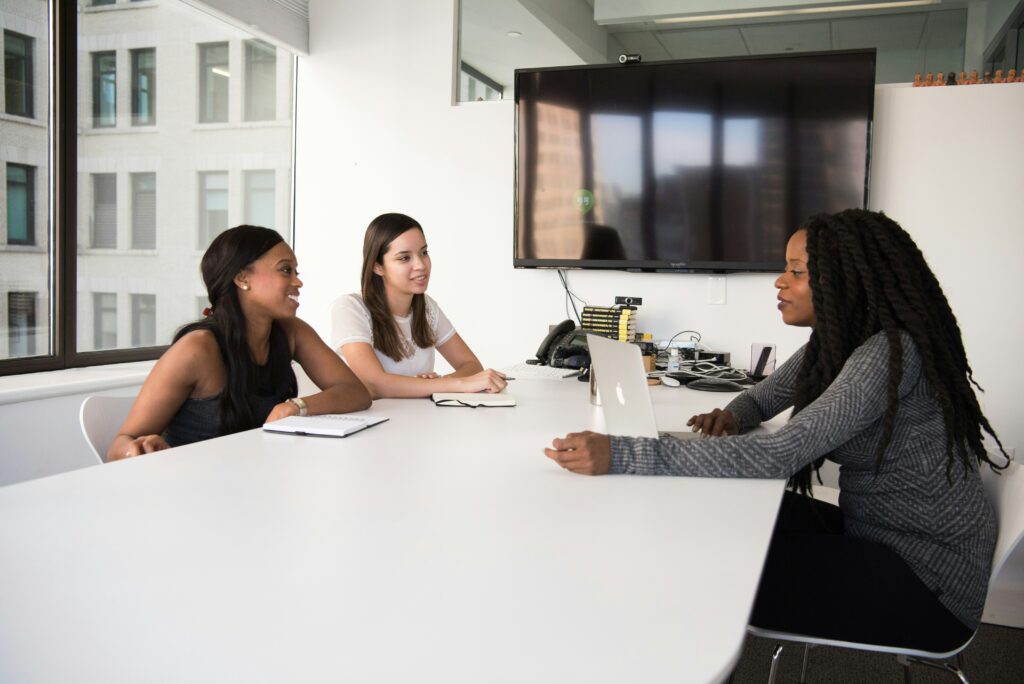 Three women sitting at a table in a business meeting (examples of inclusive job descriptions blog)