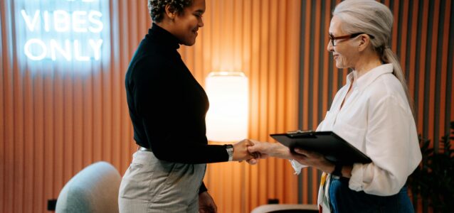 A potential candidate shaking the hand of a recruiter with the words “Good Vibes Only” in the background.