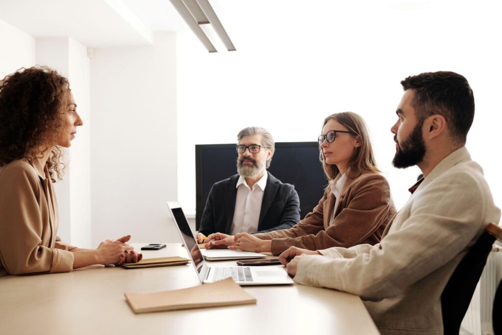 Four professionals seated around a conference table with laptops and notebooks, engaged in a meeting.