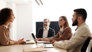 Four professionals seated around a conference table with laptops and notebooks, engaged in a meeting.